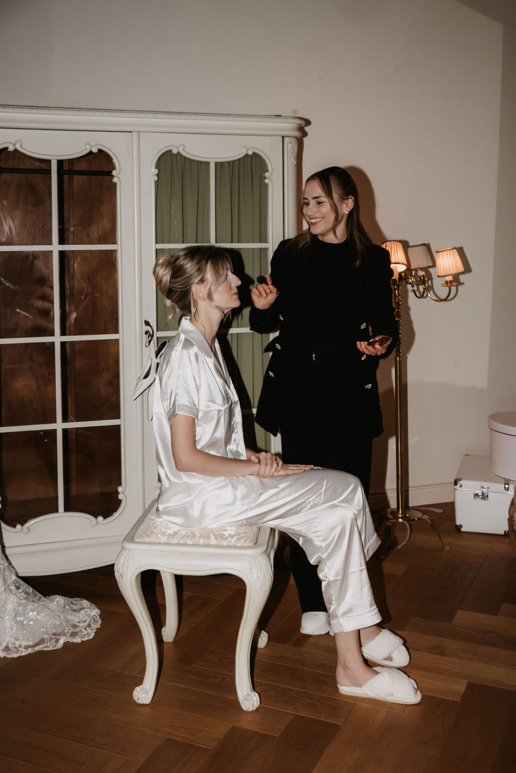Make-up Artistin schminkt eine sitzende Braut beim Getting Ready vor der Hochzeit