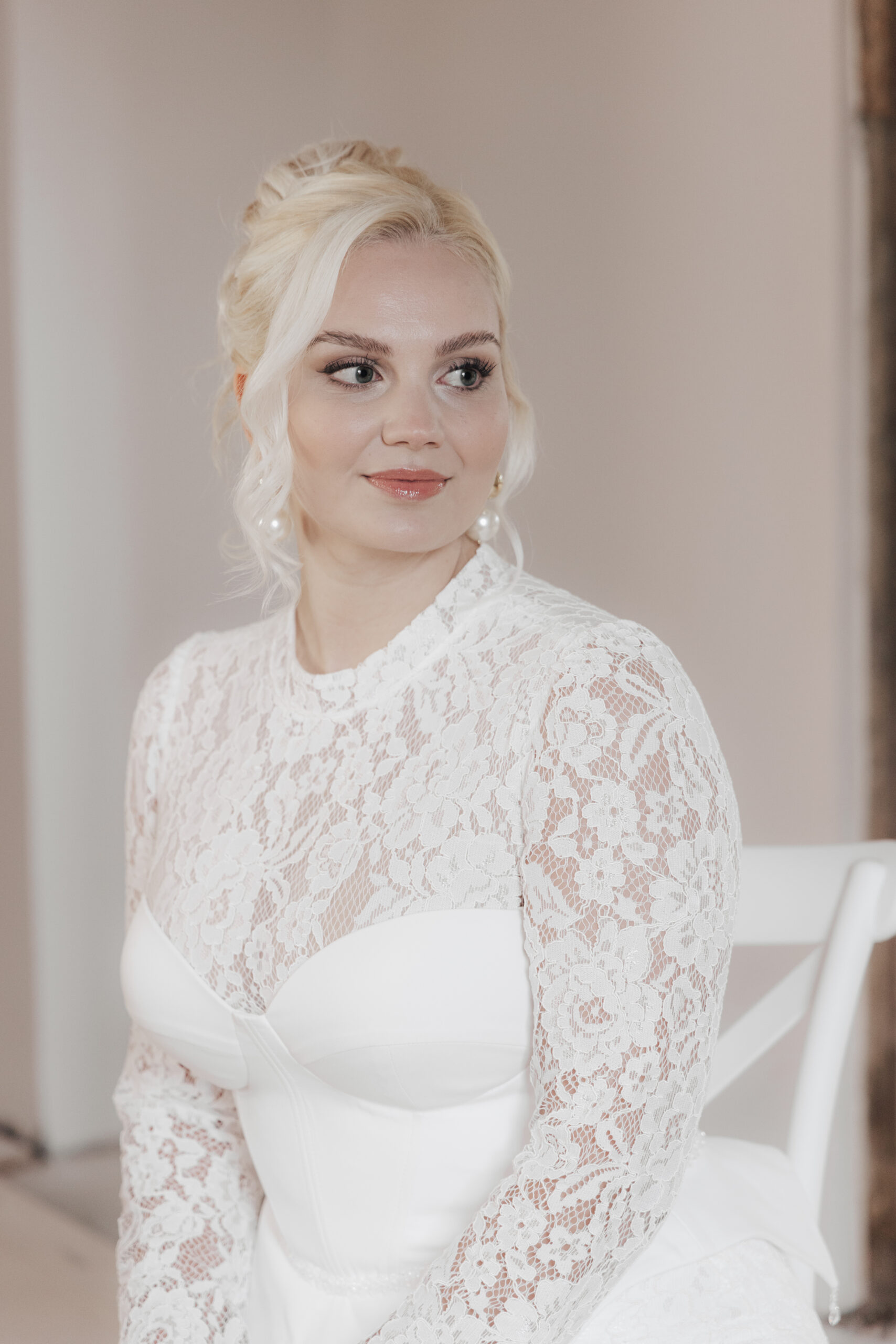 Blonde Braut mit eleganter Hochsteckfrisur, betontem Augen-Make-up und weißem Spitzenkleid